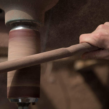 Person sanding a wooden stick with a sander