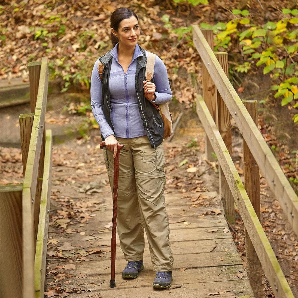 Woman with a walking stick standing on a wooden bridge in a forest