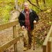 Man standing on a wooden path in a forest, holding a walking stick.