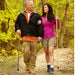 Man and woman walking together on a trail in a forest, each holding a walking stick.