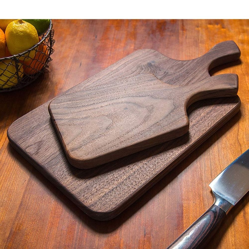 Two wooden cutting boards on a wooden surface with a knife and fruit basket in the background.