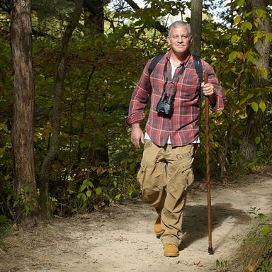 Man hiking in a forest wearing a red plaid shirt and carrying a camera.