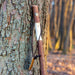 Knife with wooden handle attached to a tree trunk in a forest setting