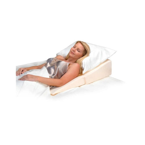 A woman reclining on a wedge bed support with a white pillow and white bedding, shown against a plain white background.