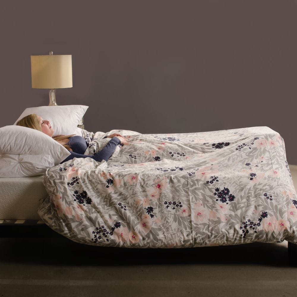 Person lying on a bed with a floral-patterned comforter in a bedroom setting.