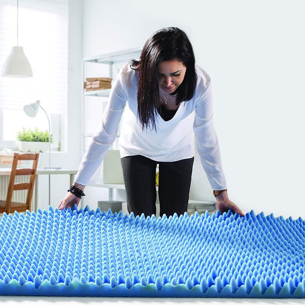 Woman examining a blue foam mattress topper in a room.