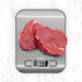 Two pieces of raw meat on a digital kitchen scale with a white marble background