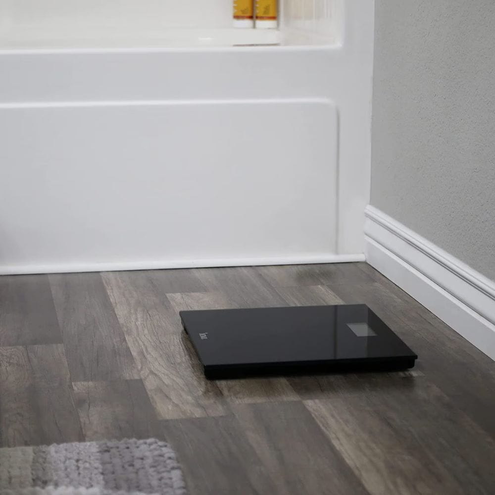 Black digital scale on a wooden floor with a neutral wall background