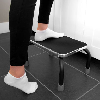 Person using a black step stool on a tiled floor