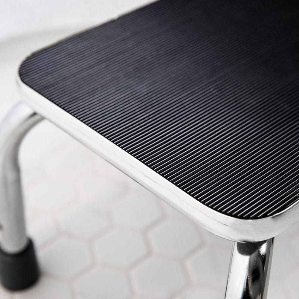 Step stool with black textured top and metal legs on a light background