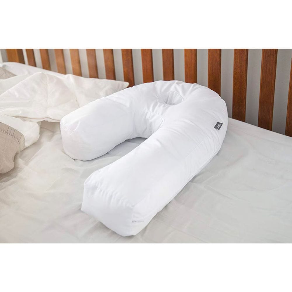A white U-shaped baby support pillow resting on a white bedsheet with a wooden slatted headboard in the background.