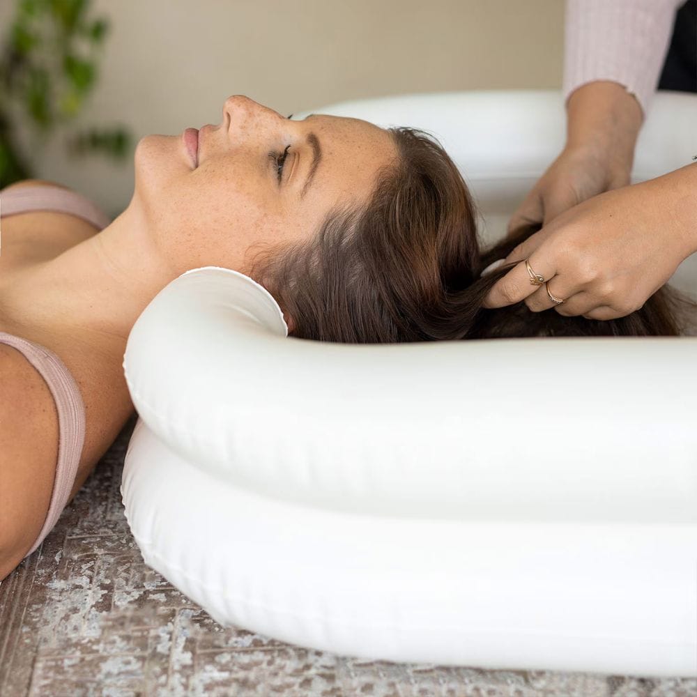 Woman receiving a hair treatment or massage on a white cushion.