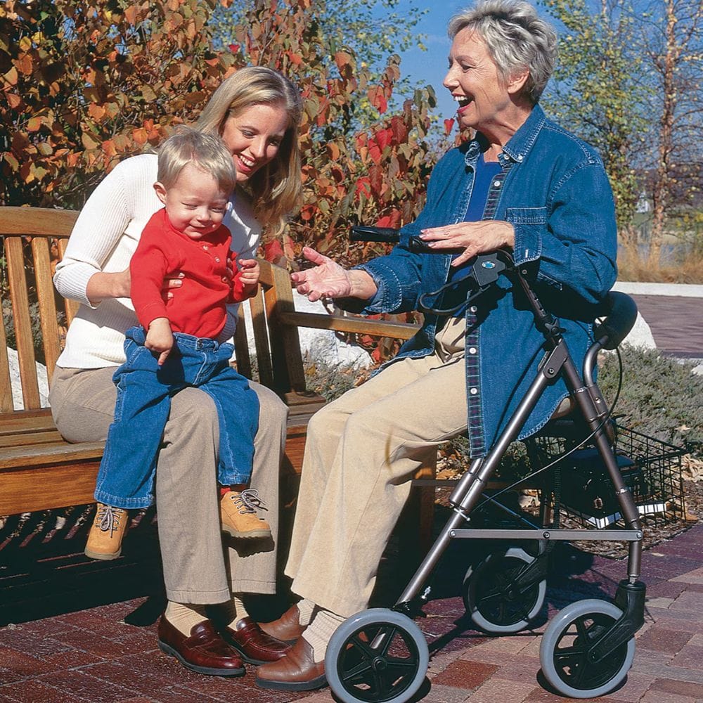 Woman holding a child next to an elderly person using a walker outdoors.