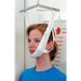 A woman wearing a white chin-lower support harness suspended from a metal frame, shown indoors against a white door and weight-measuring wall.