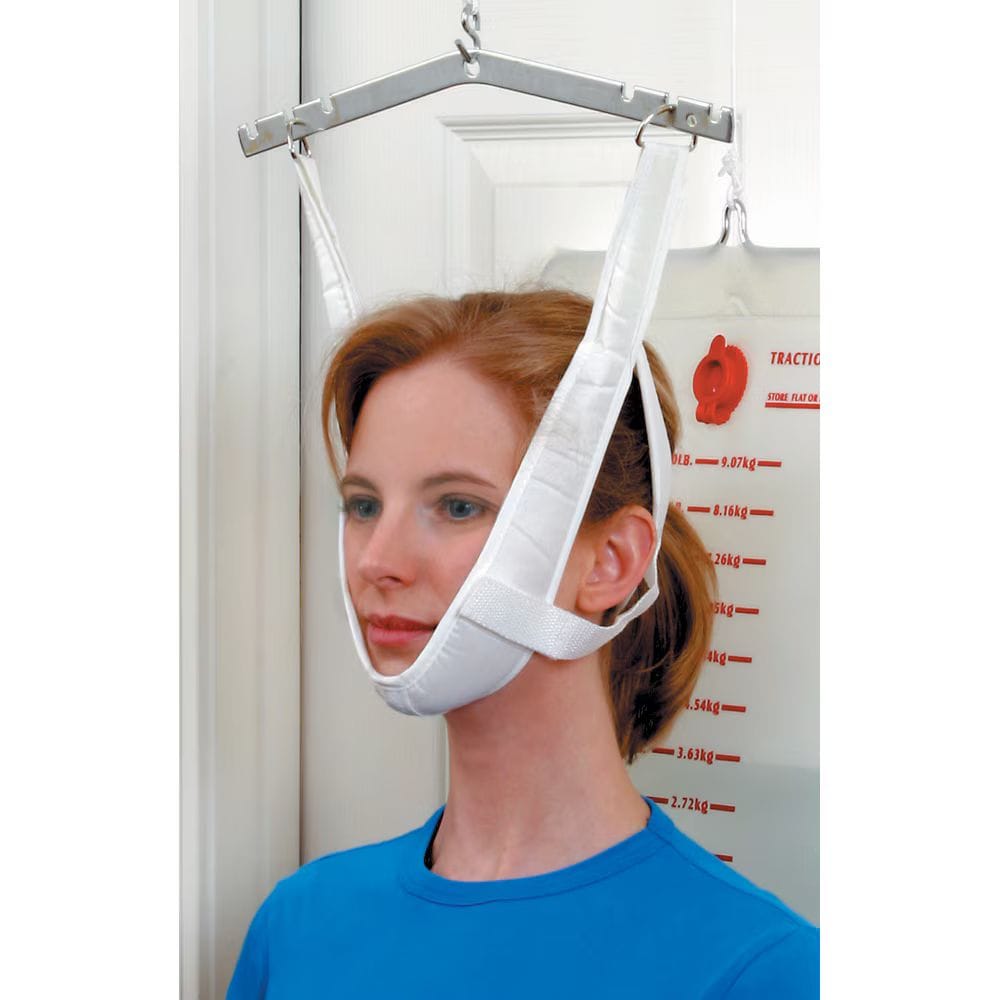 A woman wearing a white chin-lower support harness suspended from a metal frame, shown indoors against a white door and wall with measurement markings.