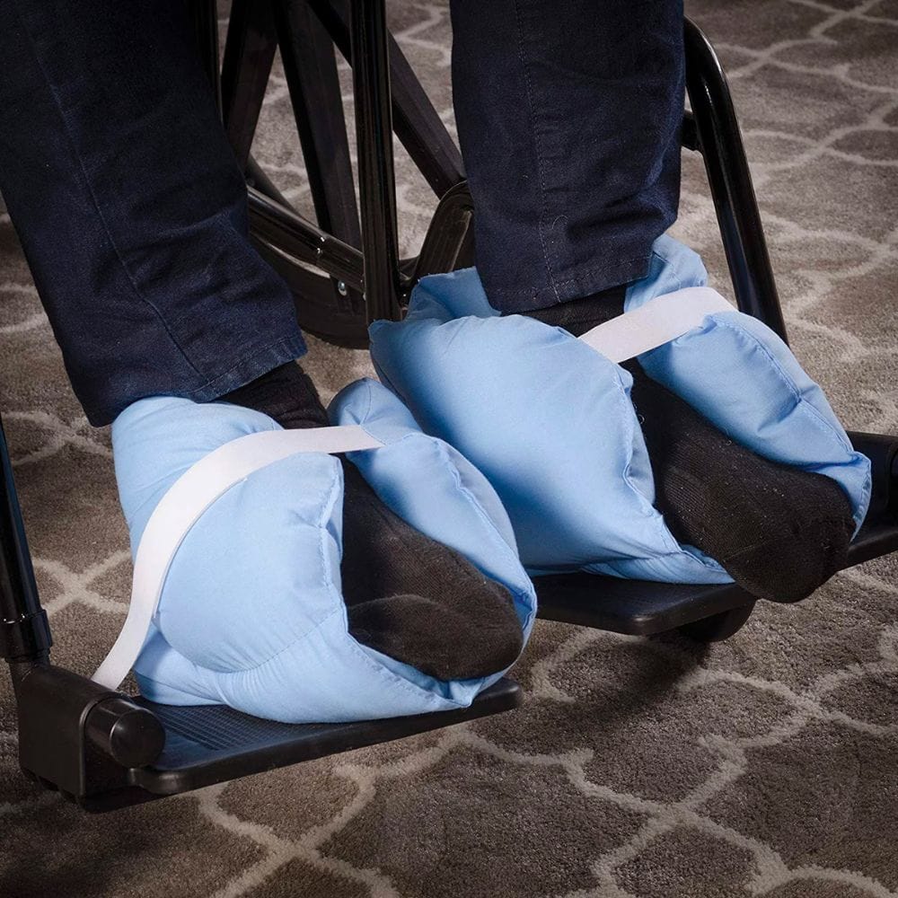 Person using a foot exerciser with blue foot sleeves on a carpeted floor.