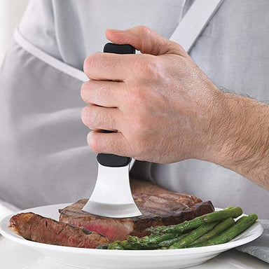 Person using a meat tenderizer on a steak with asparagus and green beans on a plate.