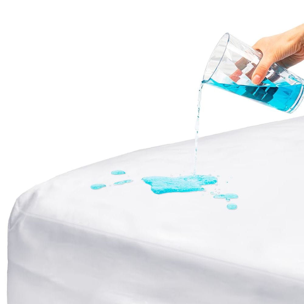 A close-up of a white bed sheet or mattress cover with blue liquid spilled on top, while a hand holds a glass pouring the liquid. The image demonstrates water resistance on a clean white background.