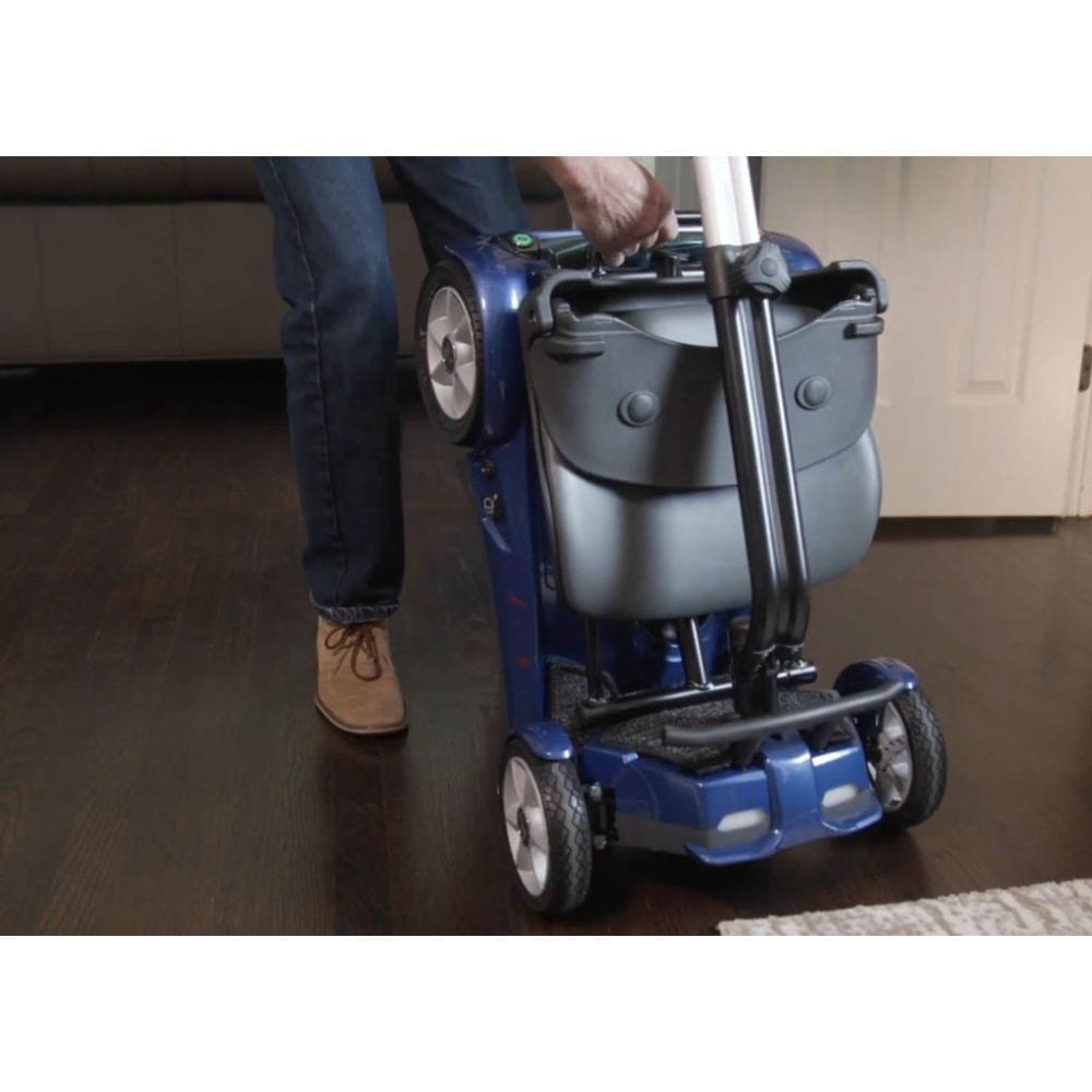 Person using a mobility scooter with a suitcase attached on a wooden floor.