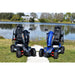 Two mobility scooters, one black and one blue, parked on grass near a lake.