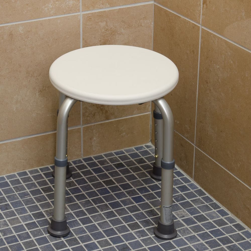 Round shower stool with white seat and metal legs in a tiled bathroom.