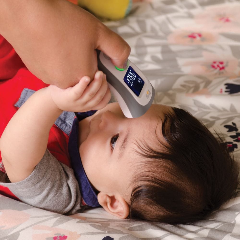 Baby lying on a bed with a digital thermometer held above its head