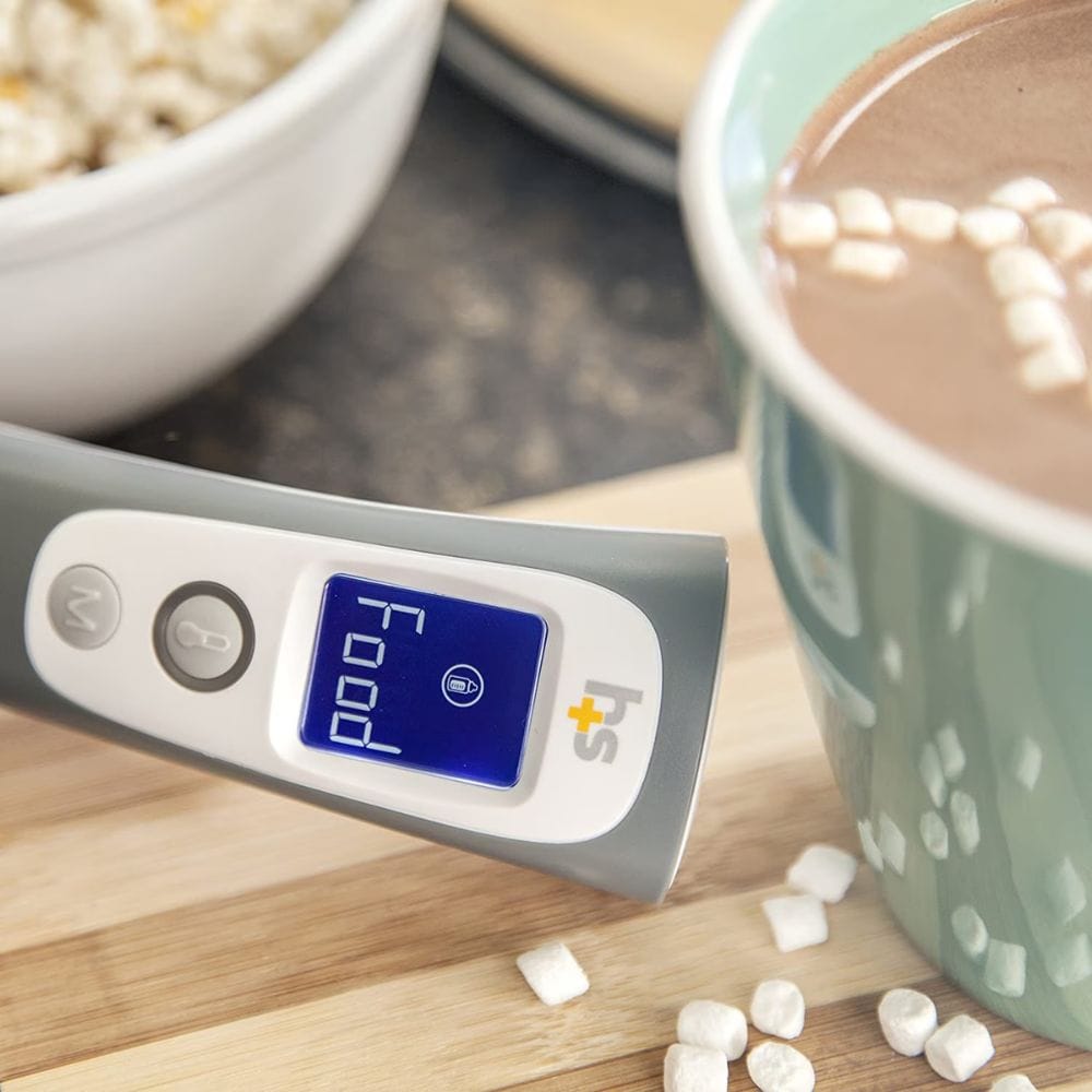 Digital thermometer on a wooden surface with a cup of hot chocolate and marshmallows.