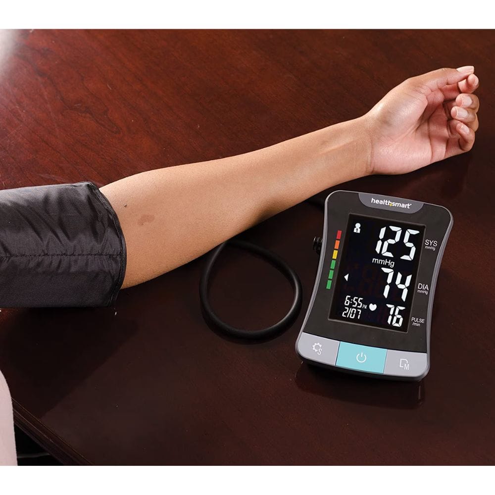 Digital blood pressure monitor on a wooden surface with a person's arm being measured.