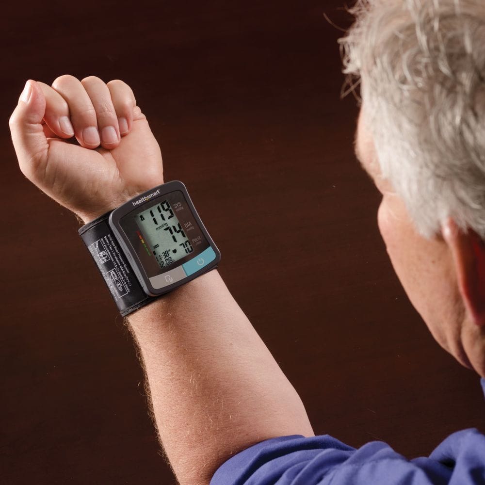 Person using a digital blood pressure monitor on their wrist with a brown background