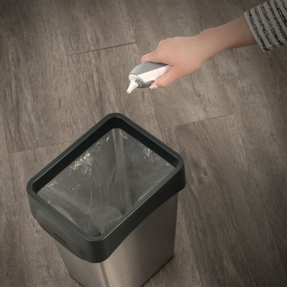 Person disposing of a used cotton pad into a trash bin on a wooden floor.