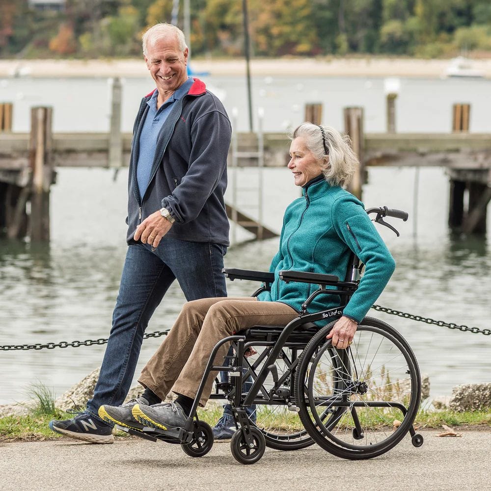 Man pushing a woman in a wheelchair by a waterfront