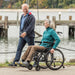 Man pushing a woman in a wheelchair by a waterfront