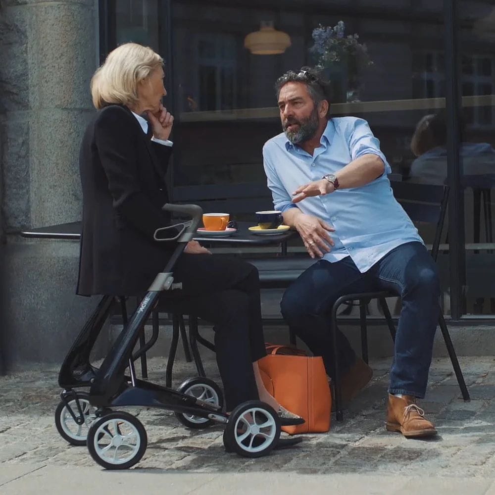Two people sitting at an outdoor cafe table with a stroller nearby.