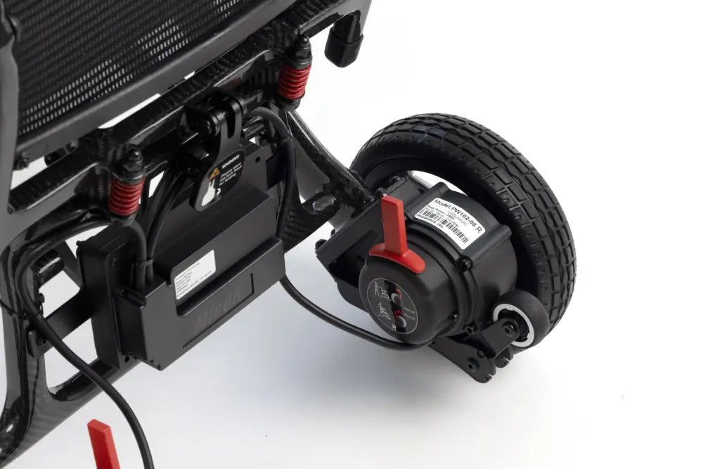 Close-up of a black electric scooter or quad bike rear suspension and wheel assembly, featuring a black tire, black motor, red handlebar lever, and red shock absorbers on a white background.