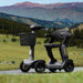 Two mobility scooters on a road with a scenic mountain background