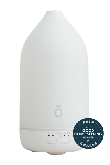 A white minimalist essential oil diffuser with a matte finish, featuring a small circular logo on the front and a dark blue 'Bath Good Housekeeping Awards 2023 Winner' badge on the lower right.