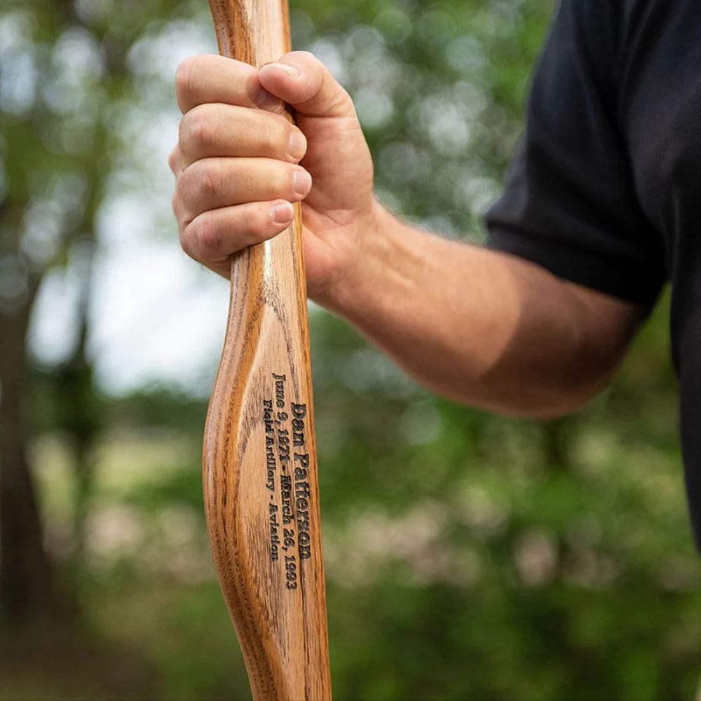 Hand holding a wooden tool with engraved text against a blurred natural background
