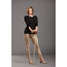 Woman wearing a black top and beige pants holding a long object against a gray background