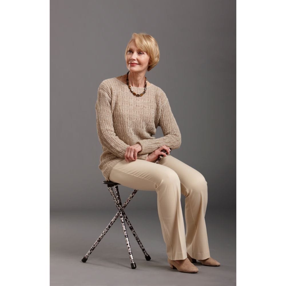 Woman sitting on a stool wearing a beige sweater and pants against a gray background