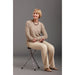 Woman sitting on a stool wearing a beige sweater and pants against a gray background