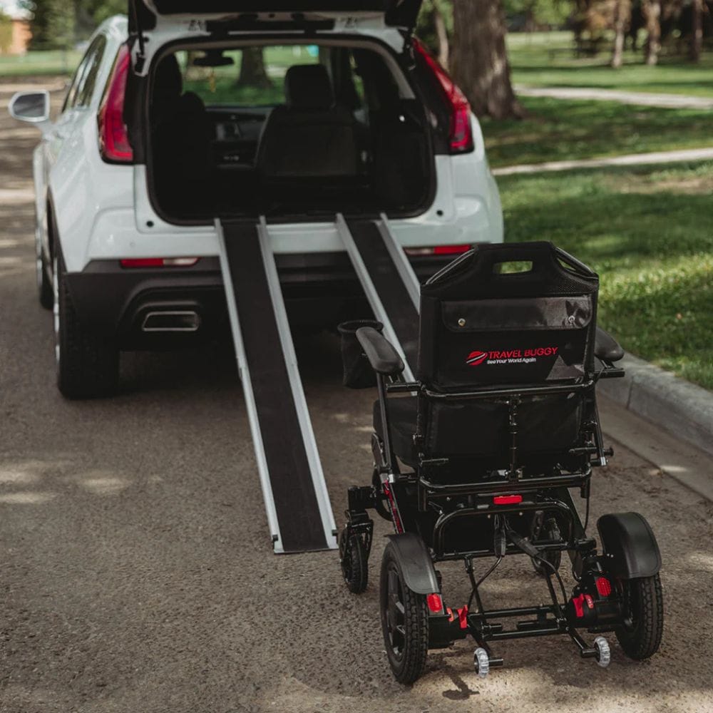 Black wheelchair with ramp attached to a white SUV in a park setting