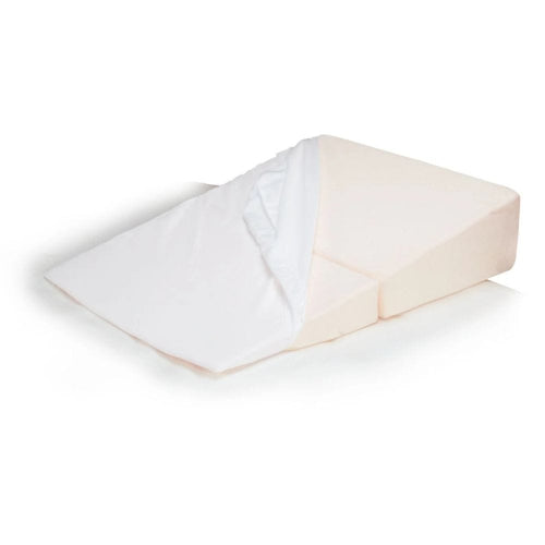A wedge-shaped orthopedic pillow in a light peach-beige color, shown with a white fitted sheet partially pulled up on one side, set against a plain white background.